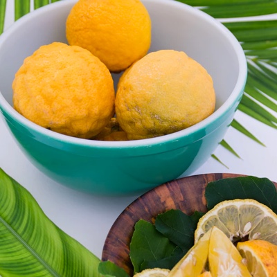 Upclose of a teal bowl with lemons on a table covered in palm leaves